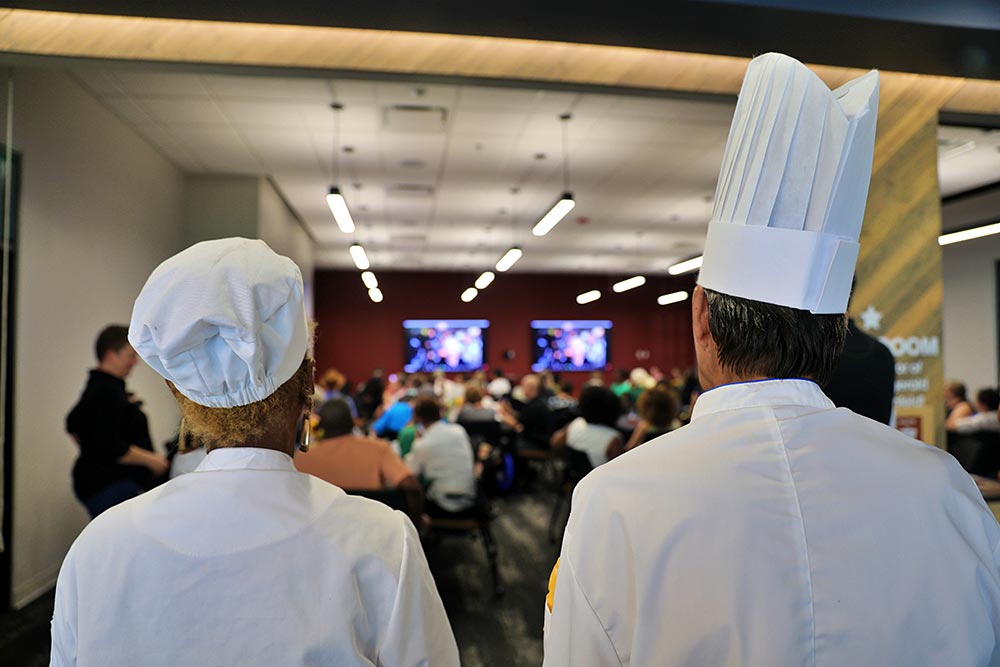 Chefs in a conference room viewing a video stream featuring Jacuqes P&eacute;pin