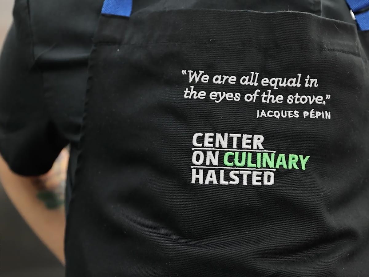 Close up of a chef apron with the phrase "We are all equal in the eyes of the stove"